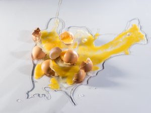 Arial view of 3 cracked raw eggs spilled on a white background