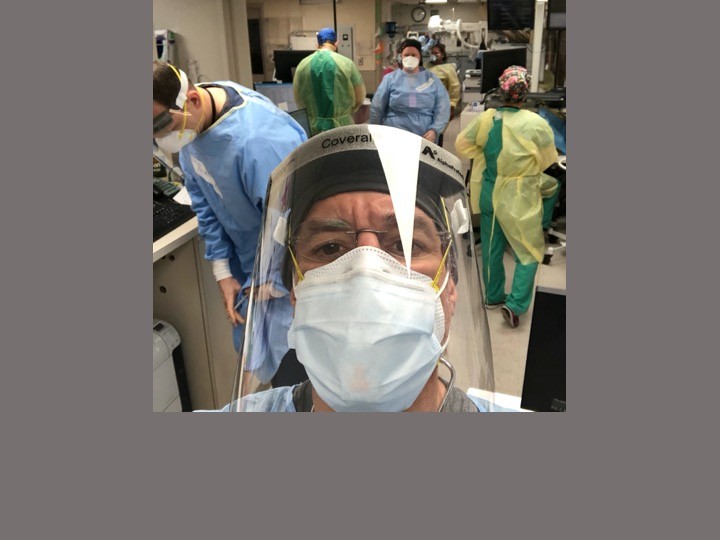 Dr. Katz in full PPE - mask and shield - and other healthcare workers in the background, working on patients