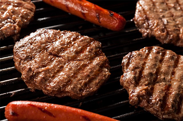 Close up of a grill with 4 hamburgers and 2 hotdogs