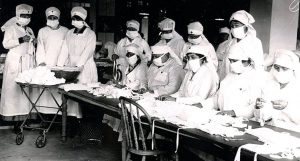 Black and white image of nurses in surgery garb folding face masks