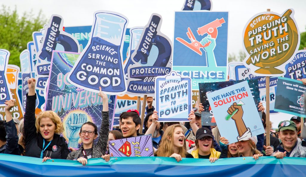 Young protestors smiling and holding up "truth" and "science" signs.