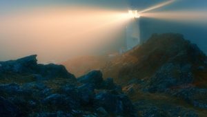 Lighthouse on a rocky hill shining through a foggy night.