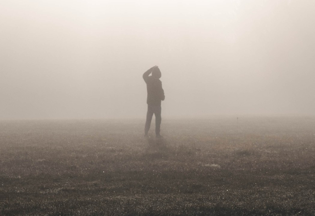 Silhouette of a person walking along a foggy field, hand scratching his/her head