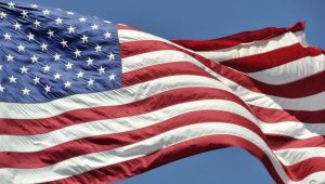 Closeup of the United States of America flag waving in the breeze, stars on the left side, on a sky blue background.