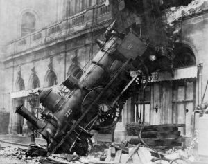 Black and white image of an early locomotive crashing into an old city building