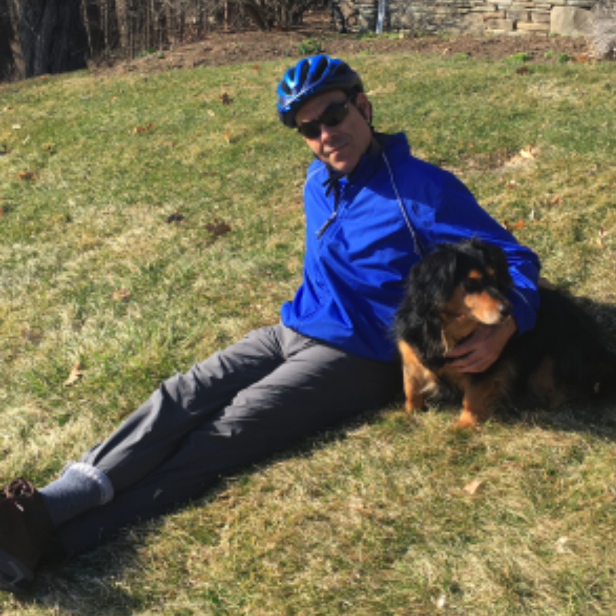Gidon Eshel wearing a blue shirt and blue bicycle helmet, sitting on hill with his dog.