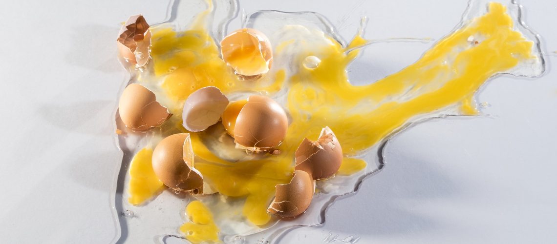 Arial view of 3 cracked raw eggs spilled on a white background